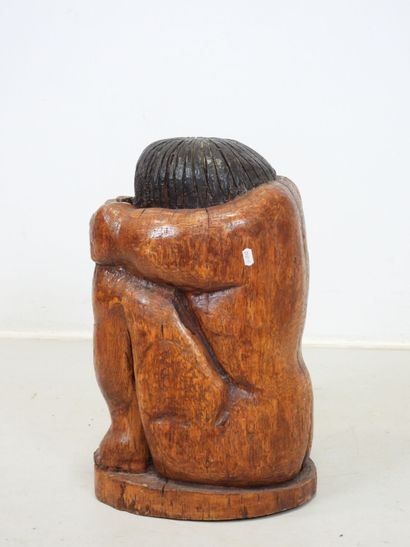 Wood sculpture of a seated, curled-up figure....