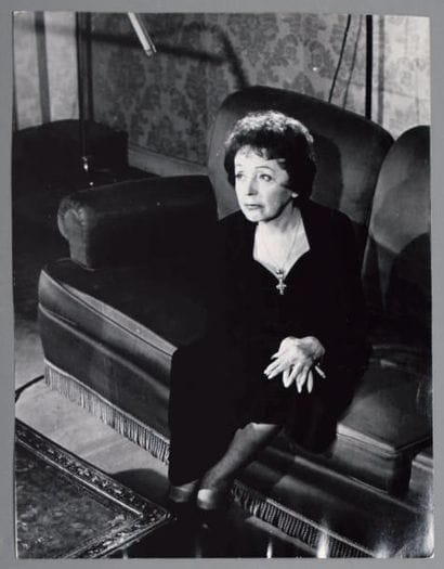 PIAF (Édith). La Chanteuse assise, dans son...