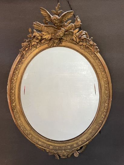 Oval mirror in wood and gilded stucco. Pediment...