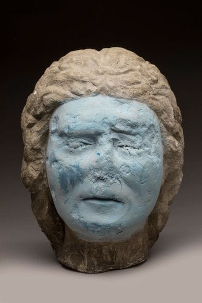 Carved limestone head; strands of hair falling...