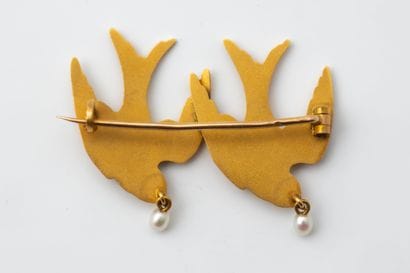 Brooch featuring two flying swallows in yellow...