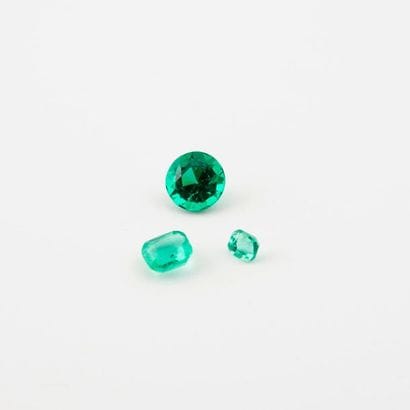 Three stones on paper, including two emeralds...